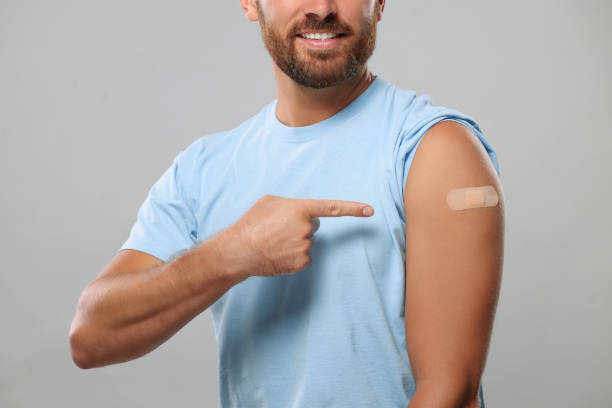 istock Man pointing at sticking plaster after vaccination on his arm against light grey background, closeup 1893575382