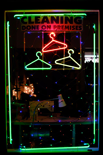 Dry cleaning front window display with neon signs at night.