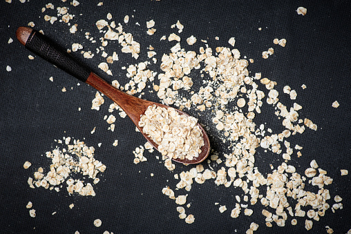 Oat flakes and wooden spoon on a black background
