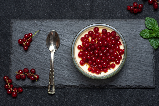 Healthy dessert with red currant jelly and yogurt, decorated with red currant, on gray background