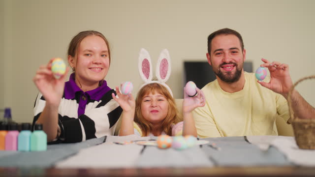 Portrait of happy young family painting Easter eggs in living room at home