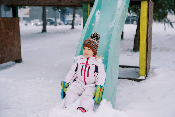 Little girl sliding down a snow-covered colorful slide. High quality photo