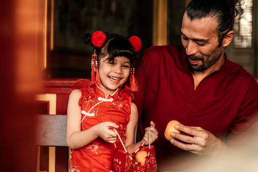 A little girl with father in traditional Chinese clothing makes a wish with oranges to celebrate the Chinese New Year