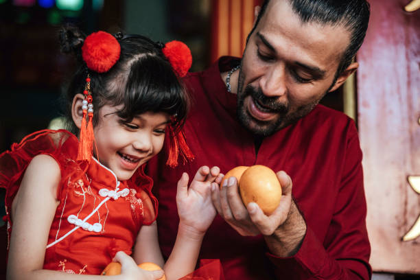 A little girl with father in traditional Chinese clothing makes a wish with oranges to celebrate the Chinese New Year