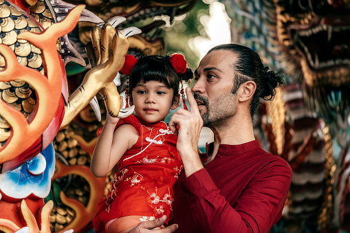 Young dad holding her lovely little daughter looking dragon sculpture in a shrine during the Chinese New Year festival