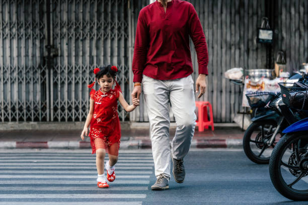 Father with little girl in traditional Chinese clothing walking outdoors in city, crossing the road
