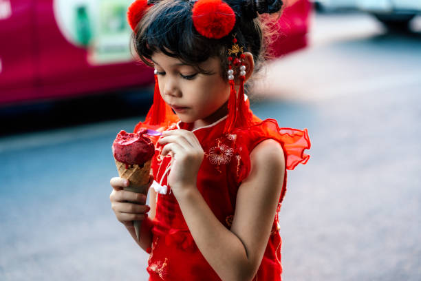 Lovely little girl in traditional Chinese clothing having ice cream cone Lovely little girl in traditional Chinese clothing having ice cream cone joyfully on street asian little chinese girls eating ice cream stock pictures, royalty-free photos & images