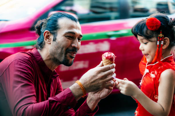 Let's eat ice cream cone! Lovely little girl with father in traditional Chinese clothing having ice cream cone joyfully on street asian little chinese girls eating ice cream stock pictures, royalty-free photos & images
