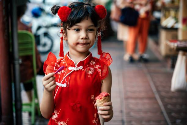 Close up of cute little girl holding ice cream Lovely little girl in traditional Chinese clothing having ice cream cone joyfully on street asian little chinese girls eating ice cream stock pictures, royalty-free photos & images