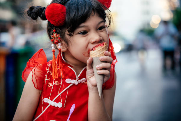 Ice Cream Lover Lovely little girl in traditional Chinese clothing having ice cream cone joyfully on street asian little chinese girls eating ice cream stock pictures, royalty-free photos & images