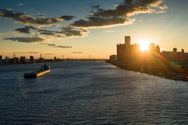 Aerial shot of the Detroit River flowing between Detroit, Michigan and Windsor, Ontario from over Belle Isle, with the sun setting behind the Detroit skyline.