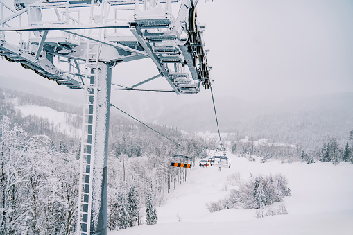Chairlift pole with chairs moving on cables uphill above a snowy forest. High quality photo