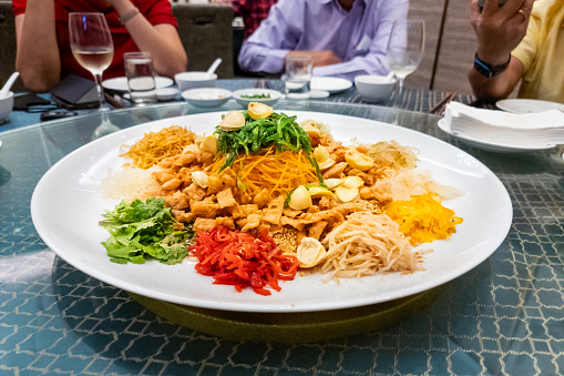 Serving of auspicious yusheng or yee sang with abalone in restaurant during Chinese New Year celebration in Malaysia with diners seated