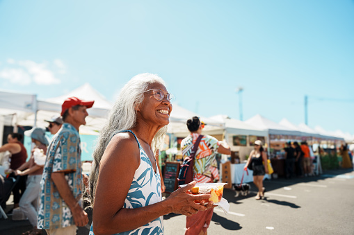 A beautiful senior woman of Hawaiian and Chinese descent smiles while exploring a farmer's market in Honolulu.