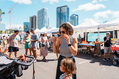 An Eurasian woman puts on her sunglasses while at the farmer's market with her preschool age daughter in Honolulu, Hawaii.