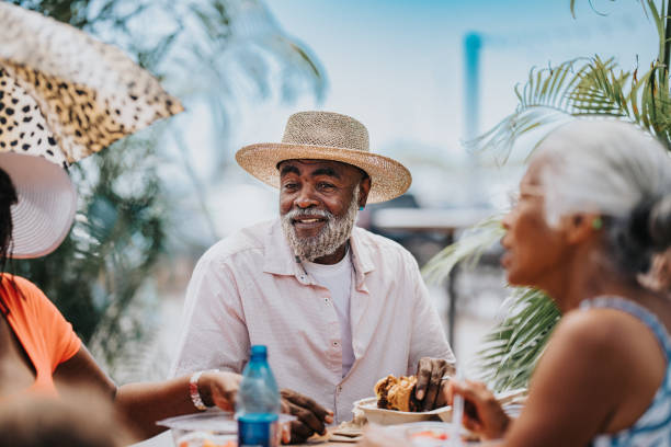 tętniący życiem starszy mężczyzna delektujący się lokalnym jedzeniem z przyjaciółmi podczas pobytu na hawajach - czarni zdjęcia i obrazy z banku zdjęć