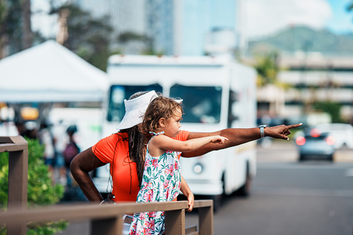 A cute Eurasian preschool age girl talks with a family friend, an African American senior woman, while at a farmer's market and food fair in Hawaii with her family.