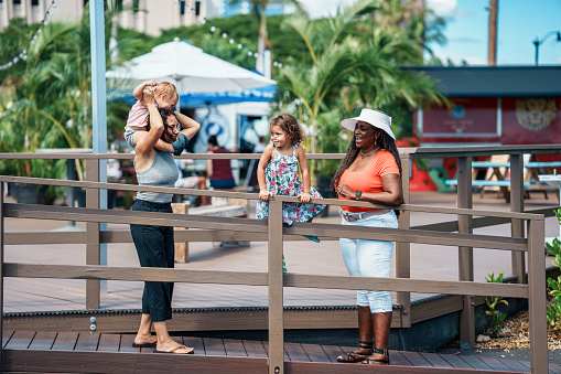 An Eurasian woman and her two young children enjoy quality time talking with a family friend, an African American senior woman, while at a farmer's market in Hawaii.