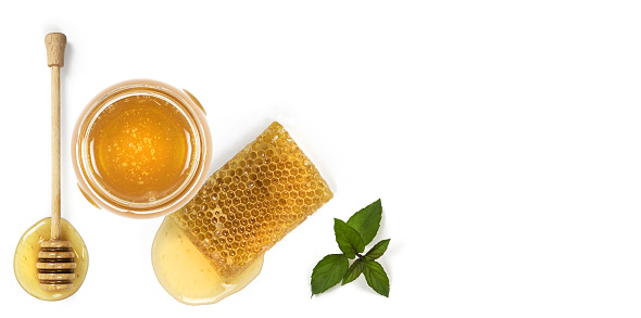 Glass of the honey, piece of bee comb, honey dipper and mint leaf on white background. View from above
