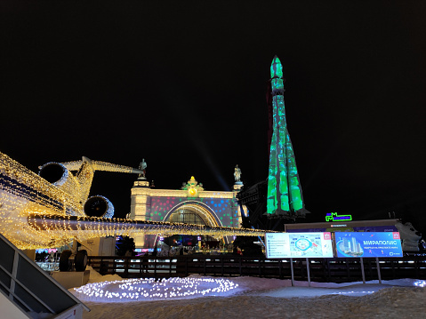 Moscow, Russia  December 23, 2023: Yak-42 aircraft in VDNKh park decorated with lights for Christmas and New Year celebration as part of the ice skating rink. Passenger plane monument with the space rocket Vostok in the background with illumination at night