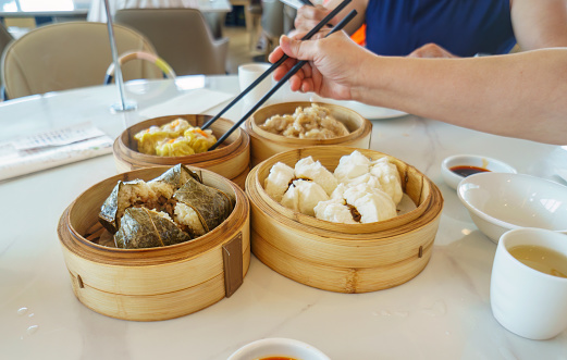 Yumcha, dim sum in bamboo steamers. Hands holding chopsticks. Selective focus on steamers in the foreground. Chinese cuisine.
