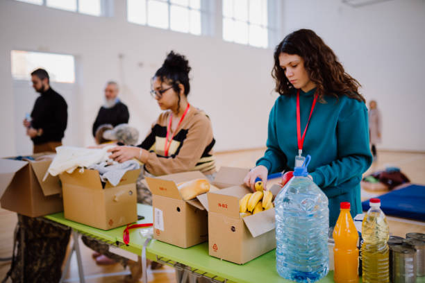 volunteers sorting, packing clothes in cardboard boxes - occupation teenager charity and relief work organized group 뉴스 사진 이미지