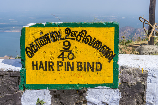 A sign indicating the 9th hair pin bend on the road from Pollachi to Valparai with the Aliyar reservoir on the background.