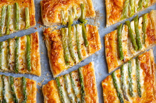 Baked green asparagus with ham and cheese in puff pastry sprinkled with sesame seeds and green basil leaves.