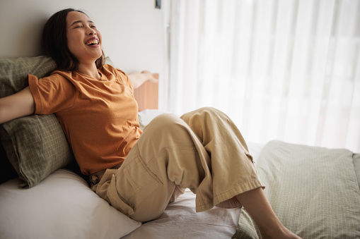 A young woman smiles cheerfully while sitiing on the bed.