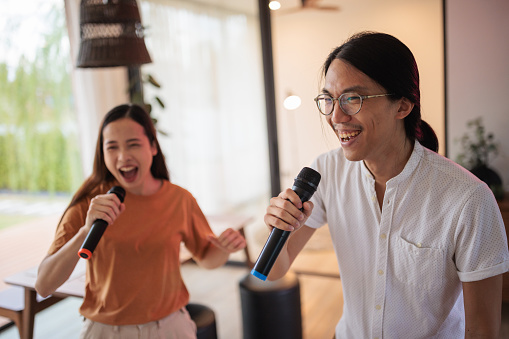 A smiling couple is singing karaoke and dancing to their favorite song together in the living room.
