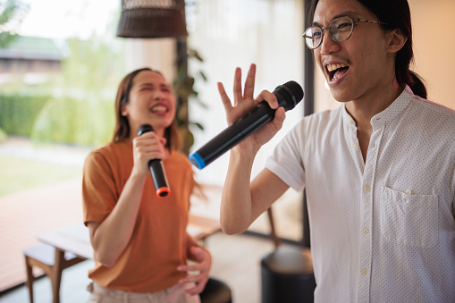 A smiling couple is singing karaoke and dancing to their favorite song together in the living room.