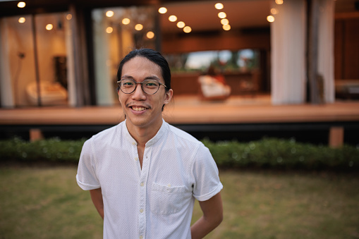 Portrait of a young man looking at the camera and smiling in front of the house at dusk.