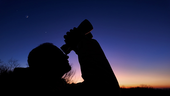 Amateur astronomer looking at the evening skies, observing planets, stars, Moon and other celestial objects with binoculars.