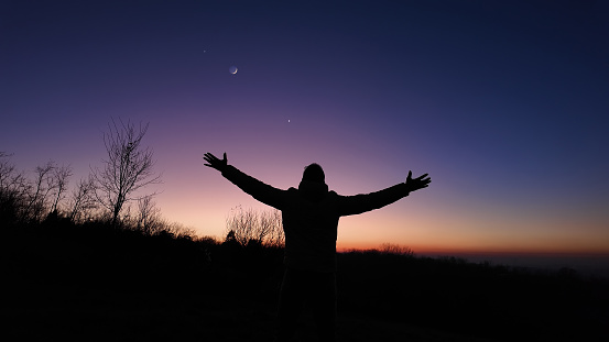 Man with arms wide open enjoying outdoors under stars, planets and Moon.