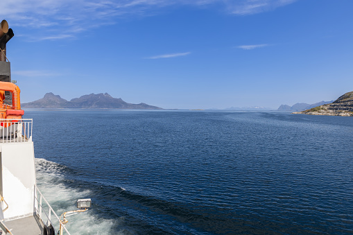 A summer view from a ferry on the North Sea towards the Lofoten Islands, showcasing the serene blue sky and the dramatic landscape of Arctic Norway