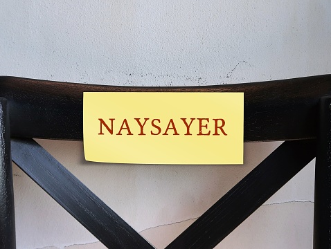 Chair back with yellow stick note written NAYSAYER concept of a person who criticizes or oppose, expresses negative or pessimistic views that something is not possible or will fail