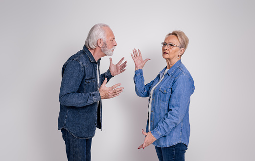 Frustrated senior wife looking away and ignoring angry husband arguing with her on white background
