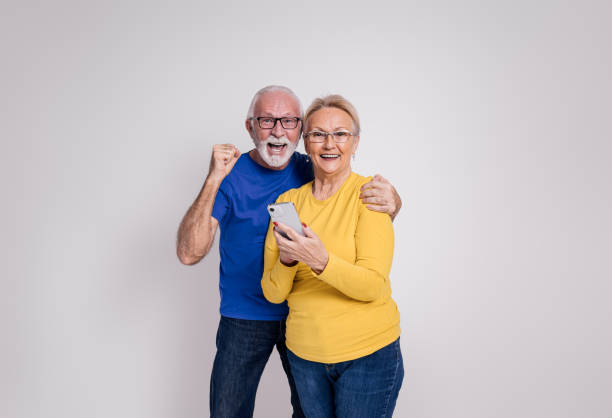 istock Smiling senior husband screaming excitedly while using smart phone with wife on white background 1894357083