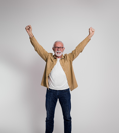 Excited senior male professional with arms raised smiling at camera and standing on white background