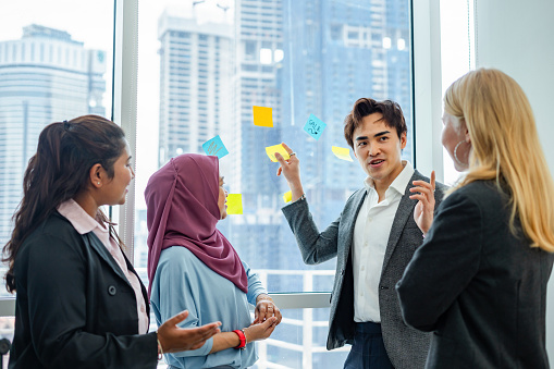 Business team discussing and brainstorming on project with sticky notes on glass in the office