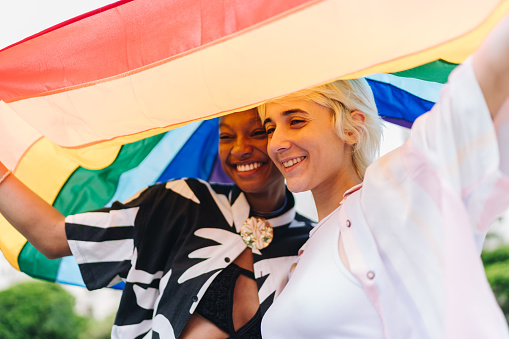 Lesbian couple embracing with rainbow flag on background