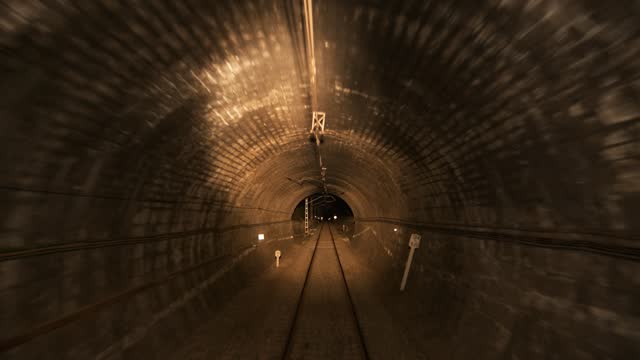 Railroad tracks and running train in tunnel near electric poles in dark night