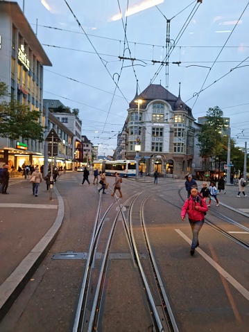 In the Center of the City district Oerlikon in Zurich. The image shows several people walking on a street behind a cable car.