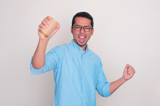 Adult Asian man clenched fist showing excited expression while holding a drink can