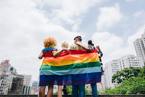Lgbtqia+ friends embracing and holding a rainbow flag outdoors