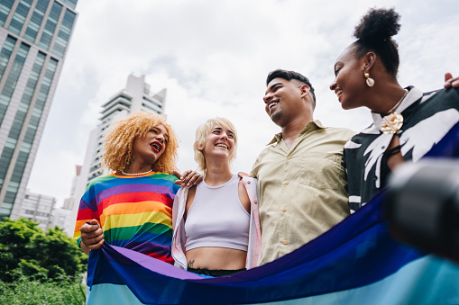 Young lgbtqia+ friends talking and holding a rainbow flag outdoors