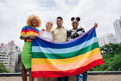 Portrait of a lgbtqia+ friends holding a rainbow flag outdoors