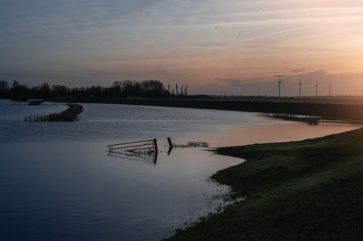 High water held back by dike with spinning windmills in distance