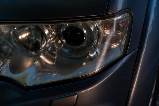 Close up on car headlights. The glass coating on the headlight surface is cloudy. Night light in the evening.