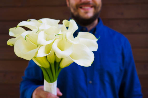 man holding many blooming white callas flowers. a bouquet of white callas lies. beautiful bouquet of white tender callas. - callas zdjęcia i obrazy z banku zdjęć